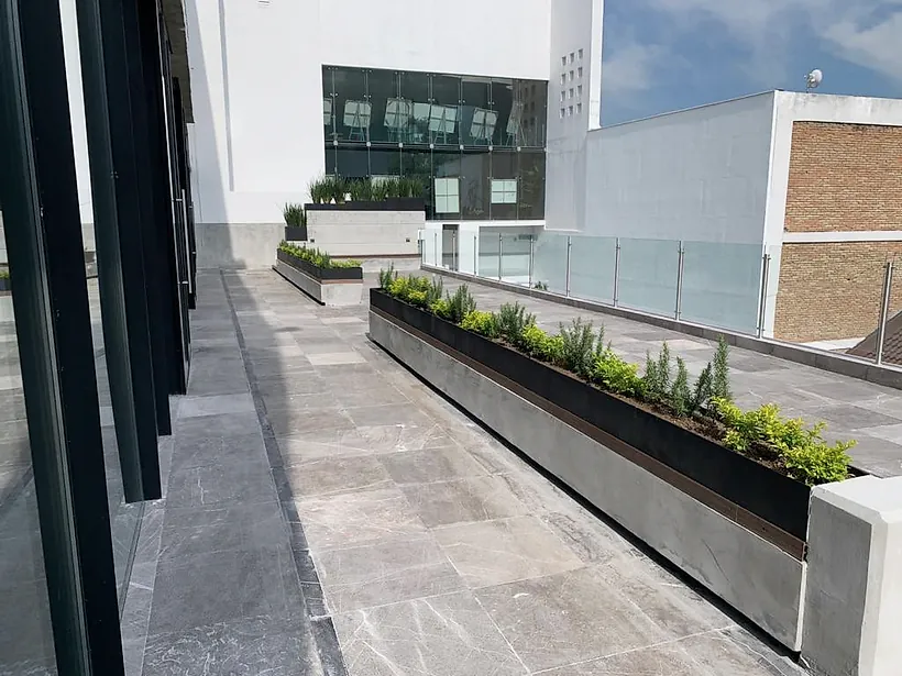 Terraza terminada del Club Alpino Chipinque: piso de piedra gris veteada, jardineras de concreto y barandal de cristal