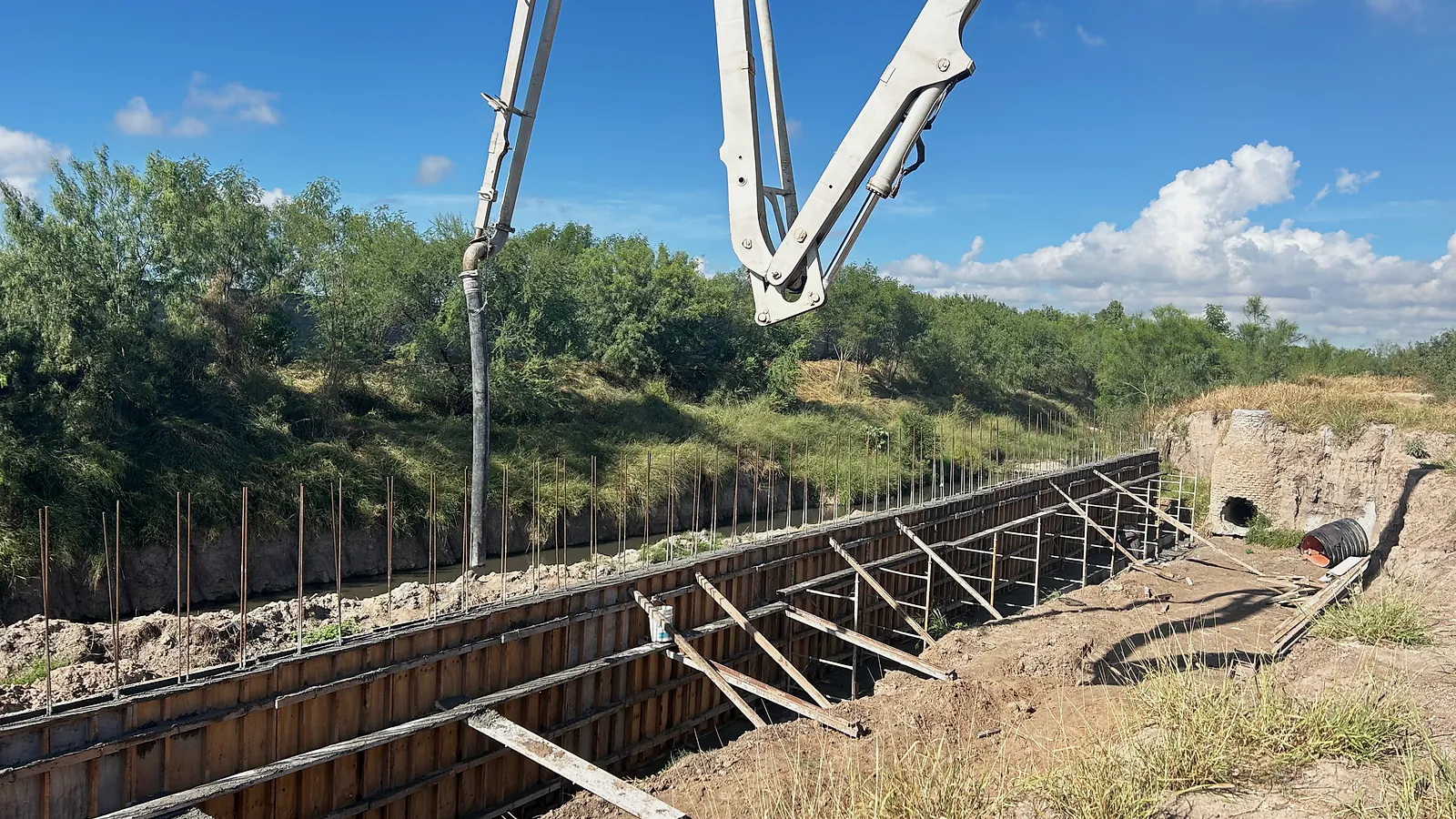Cimbra de madera troquelada del muro a lo largo del Dren El Anhelo, junto a un pozo de visita de tabique y un tubo corrugado, con la pluma de una bomba de concreto