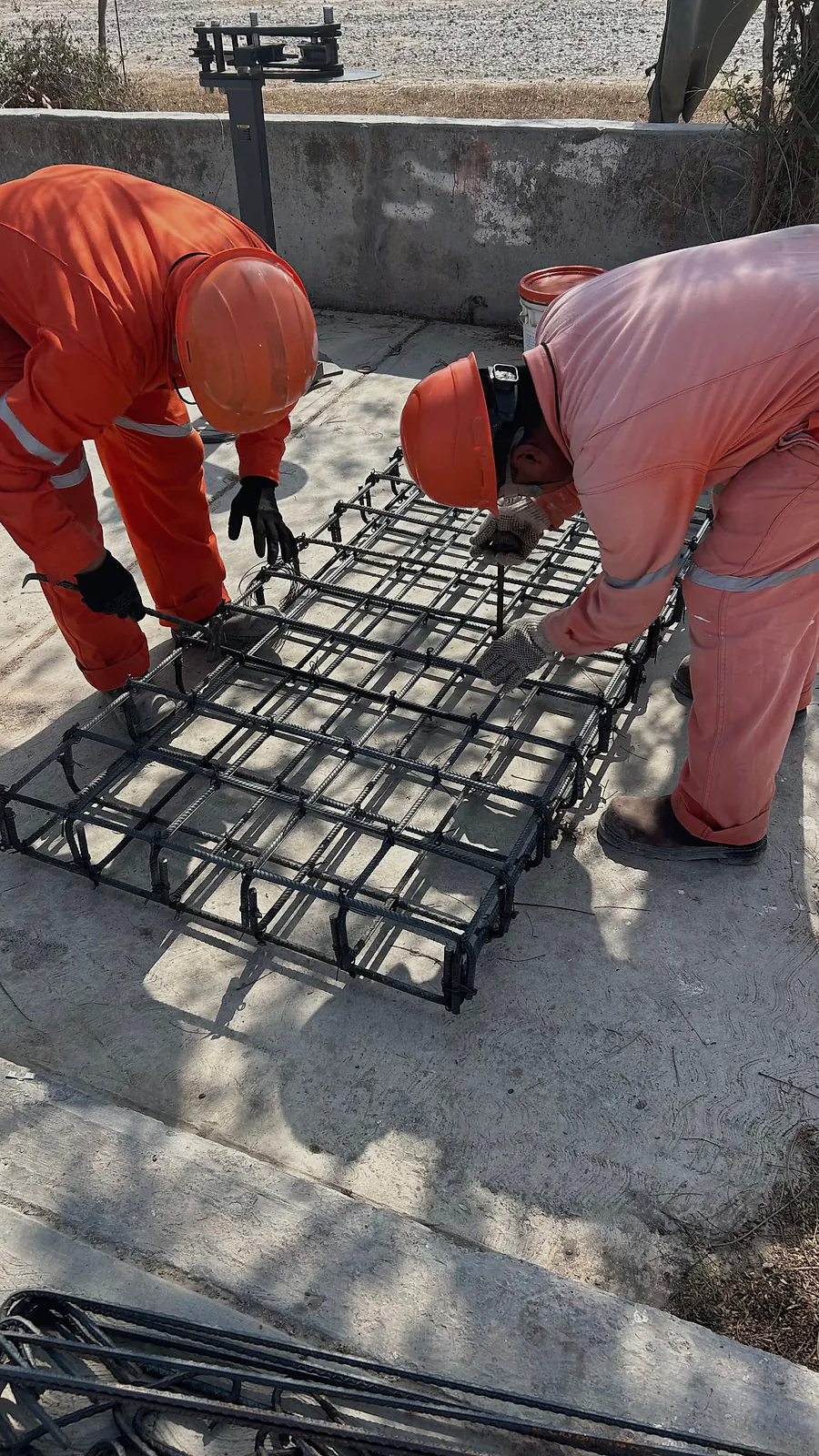 Dos trabajadores de overol naranja arman con alambre una parrilla de varilla sobre un firme de concreto, en el gasoducto Libramiento Reynosa