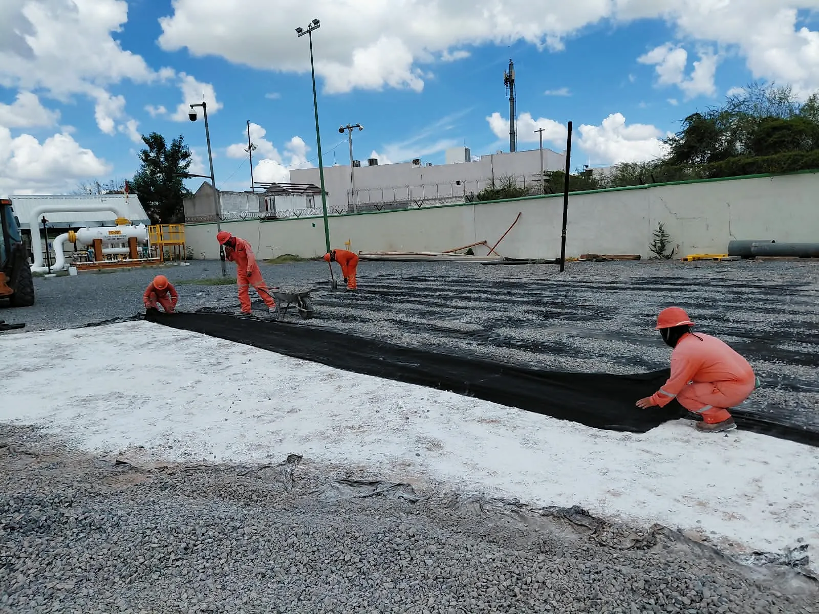 Cuadrilla de overol naranja tiende malla geotextil sobre el terreno antes de la grava, en el patio de la Terminal 02