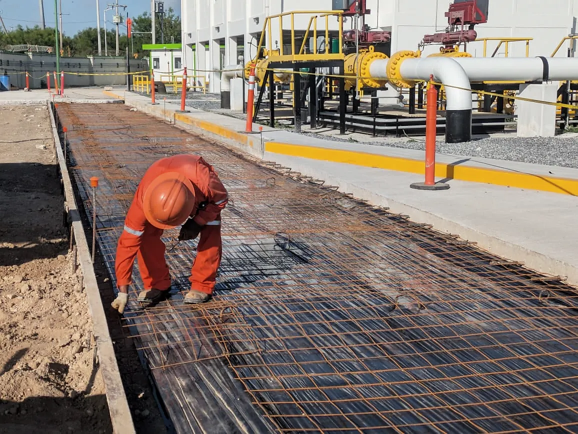 Un trabajador de overol naranja amarra la malla electrosoldada sobre el plástico de una vialidad antes del colado, en la Terminal 02