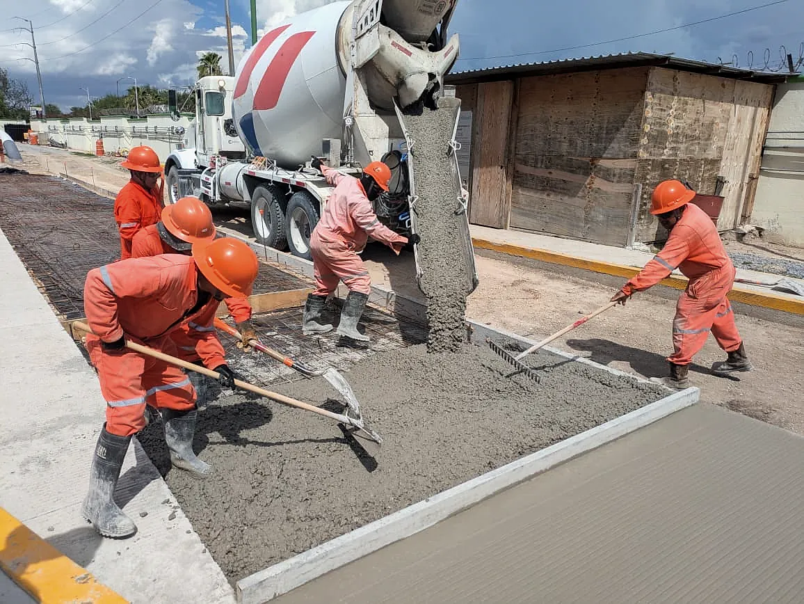 Una revolvedora descarga concreto en una vialidad mientras la cuadrilla de overol naranja lo extiende con rastrillos y palas, en la Terminal 02