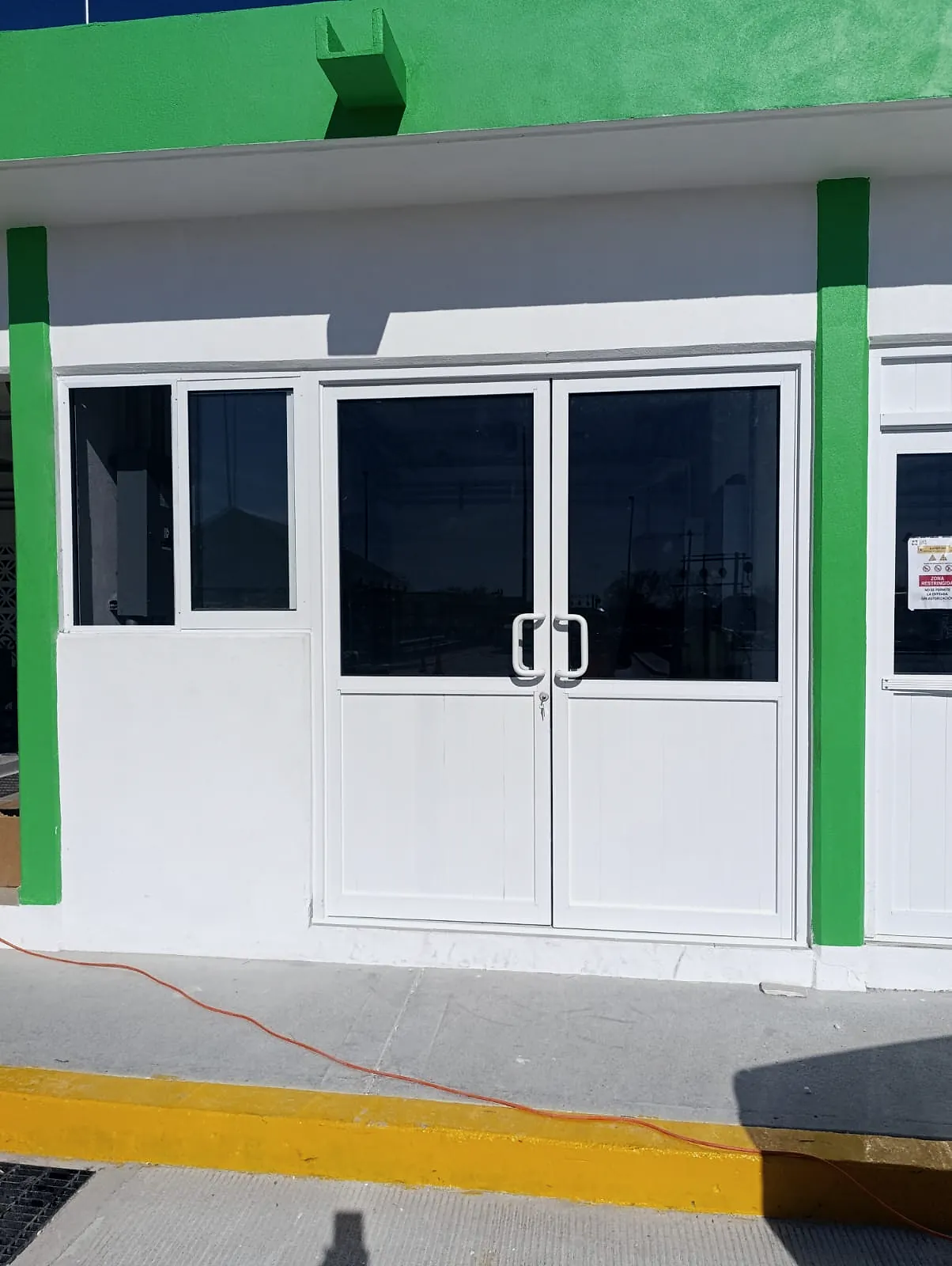 Puerta doble y ventanas de aluminio blanco en un cuarto de servicios de muros blancos y verdes, con la guarnición amarilla al frente, en la Estación Anzalduas