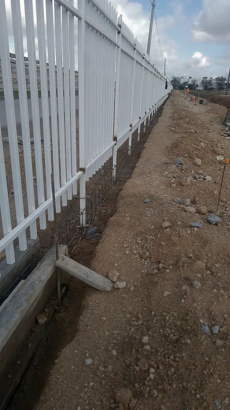 Reja perimetral de perfiles blancos sobre un murete en construcción, con el acero de refuerzo a la vista, en la Nave Dicex